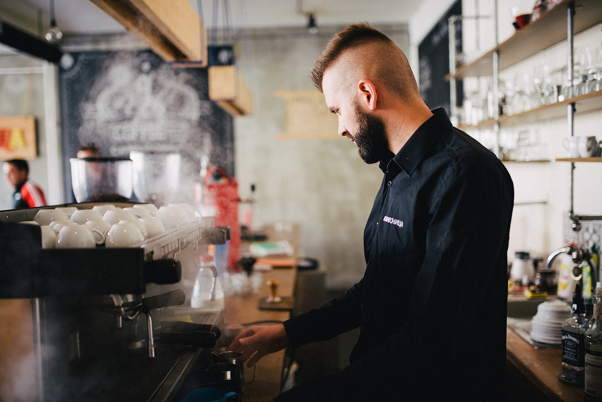 A barista steaming milk at a busy espresso machine in a modern café.