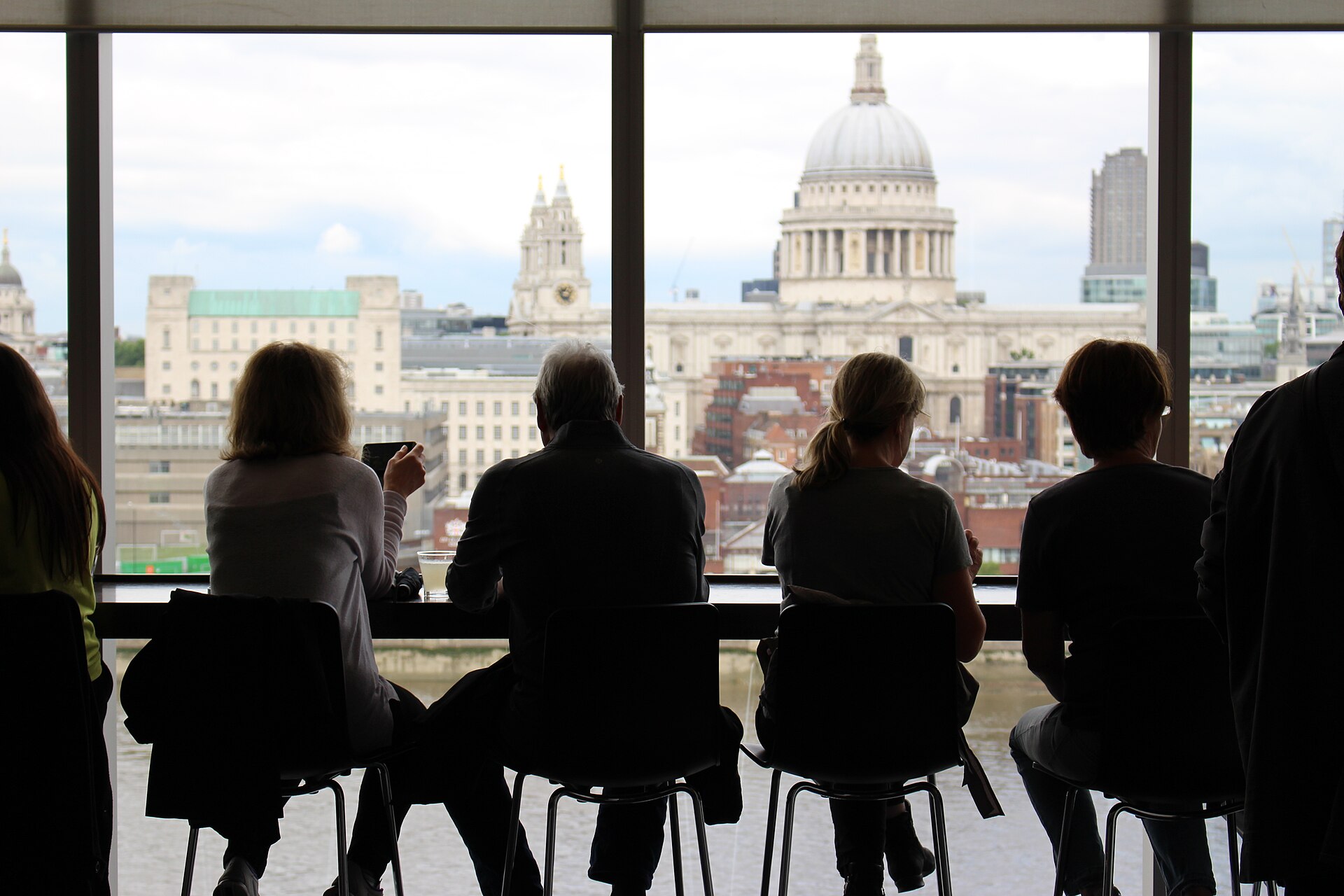 Guests on high stools along a window counter looking out over the city.